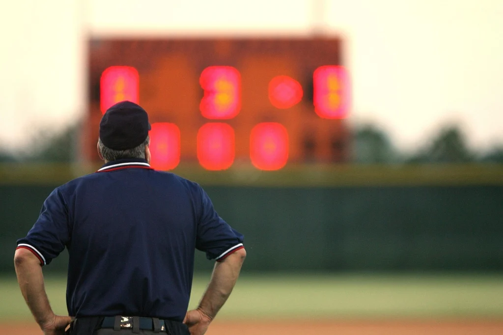 Campo de béisbol infantil al atardecer con un umpire arrodillado frente a un niño